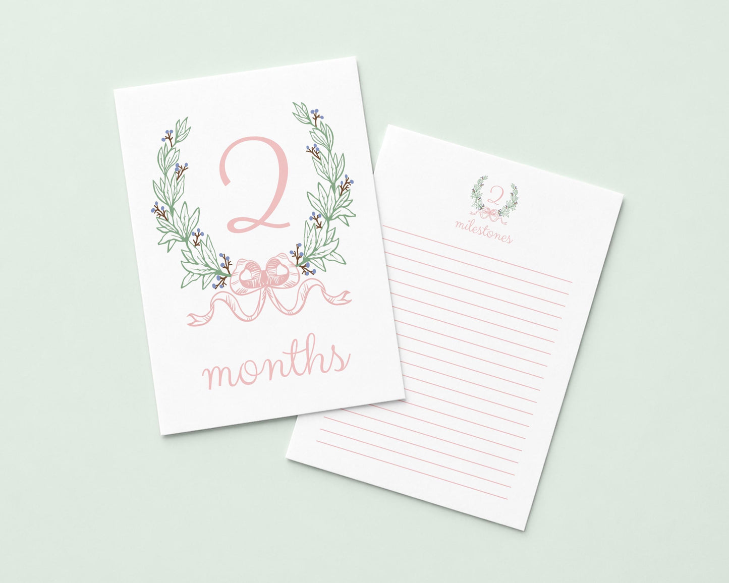 a white card with a pink floral design and the number "2" on it, along with the text " Months" written below. The card is placed next to a blank lined paper, suggesting it could be used for writing or note-taking.