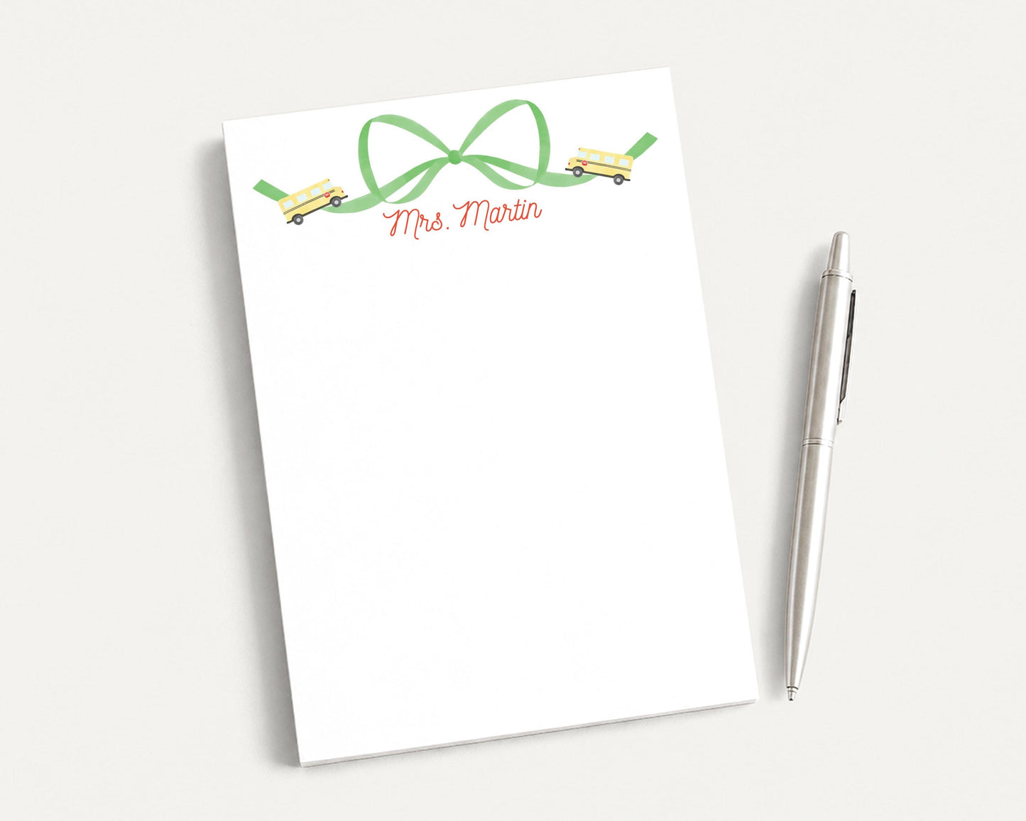 A white notepad with a green bow and a pen on a white surface.