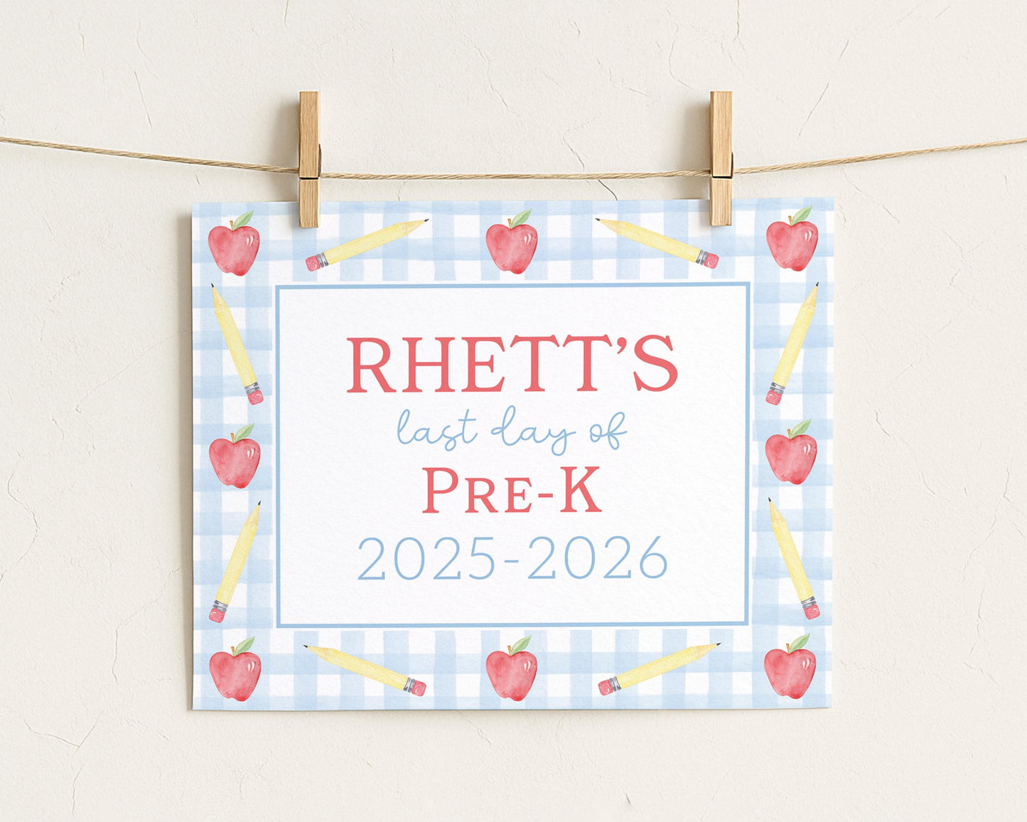 A sign with the text "RHETT'S last day of PRE-K" and "2025-2026" printed on it, surrounded by pencils and apples on a blue and white checkered background.