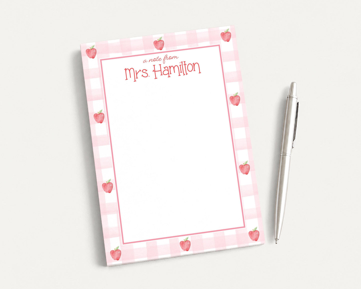 A pink and white checkered notepad with a blank page and a pen on a white surface.