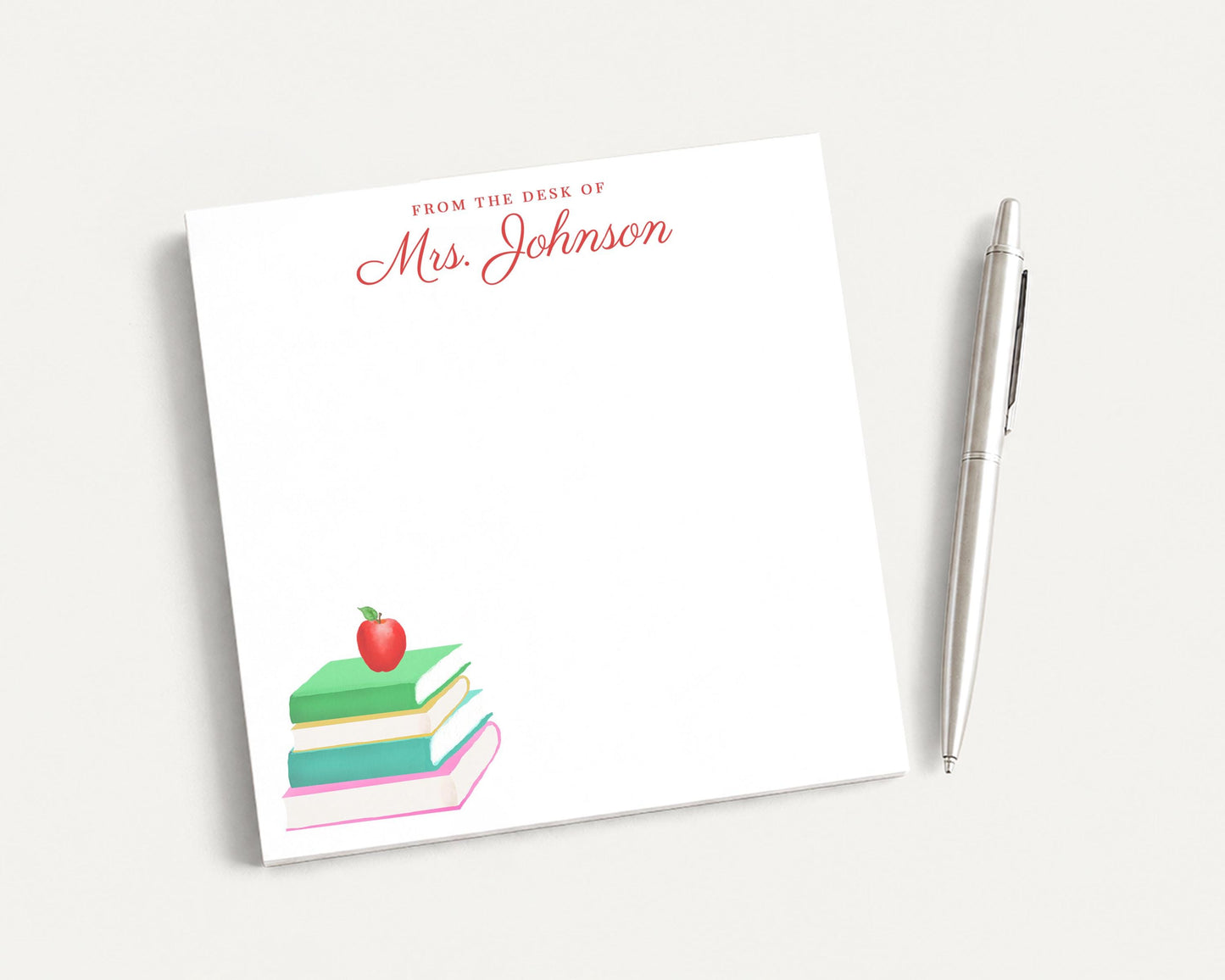 a white sticky note with a stack of colorful books and an apple on top, along with a pen.