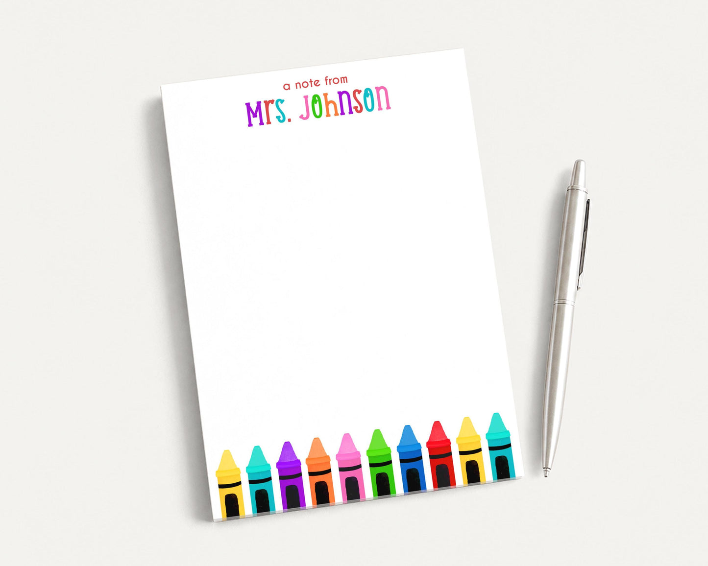 A blank white notepad with a colorful crayon design and a pen on a white surface.