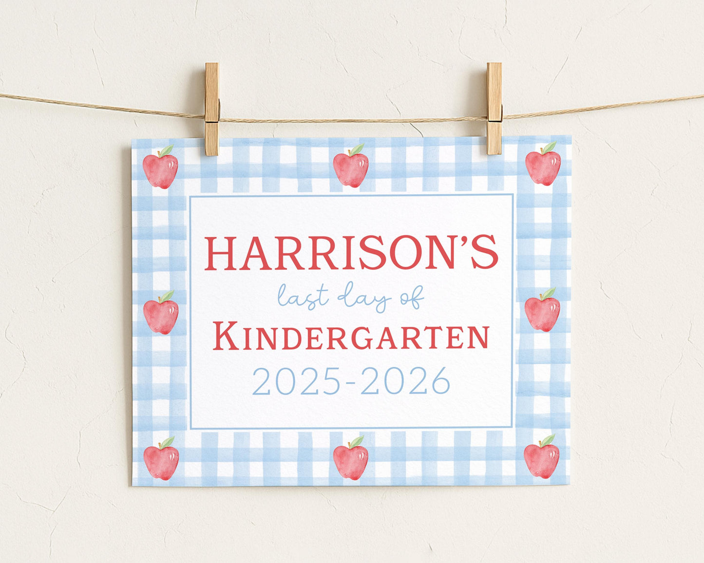 A sign with the text "HARRISON'S last day of KINDERGARTEN" and "2025-2026" printed on it, with a blue and white checkered background and red apples.