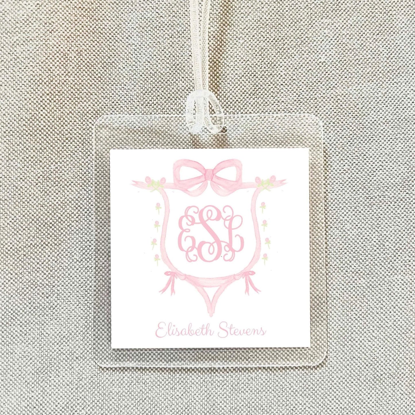 A clear plastic luggage tag with a pink monogram design and the name "Elisabeth Stevens" printed on it.