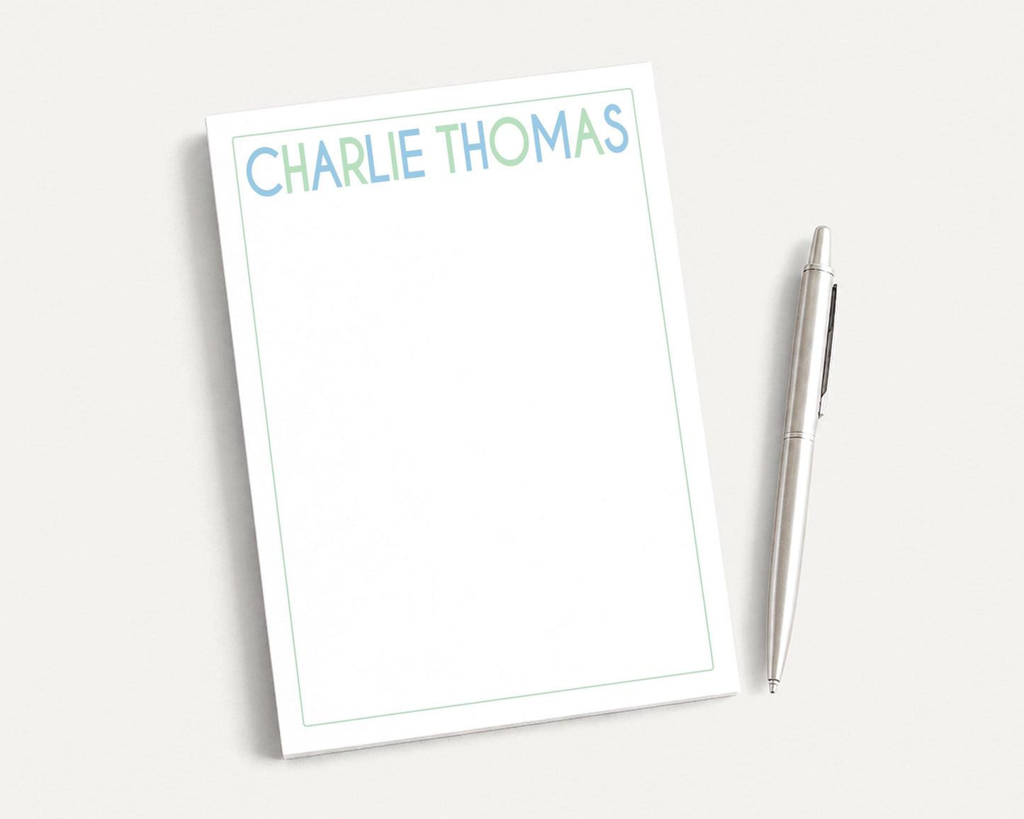 a blank white notepad with the name "CHARLIE THOMAS" written on it, accompanied by a silver pen.