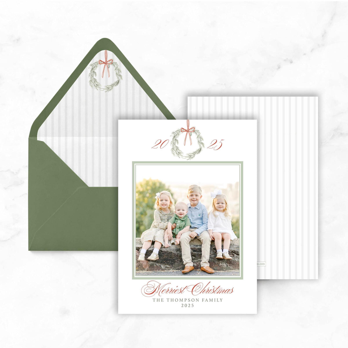 A white card with a photo of four children sitting on a rock, surrounded by greenery, and a green envelope with a wreath on top.