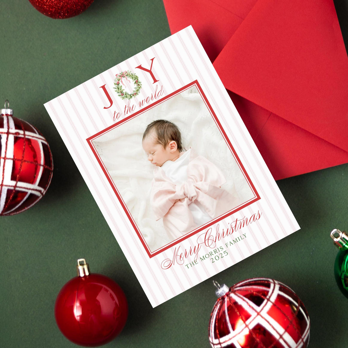 a Christmas card with a photo of a baby, surrounded by ornaments and a red ribbon on a green background.