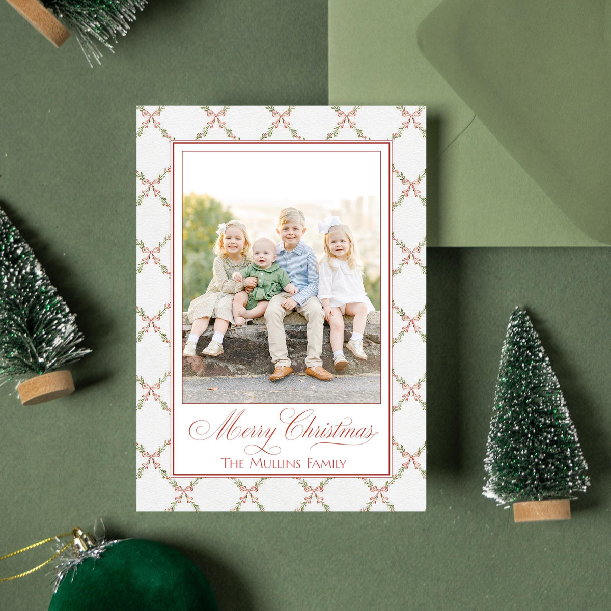 a Christmas card with a photo of three children sitting on a bench, surrounded by green Christmas trees and ornaments.