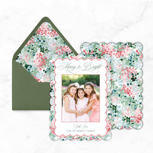 A green envelope with a floral pattern and a scalloped frame containing a photo of three young girls.