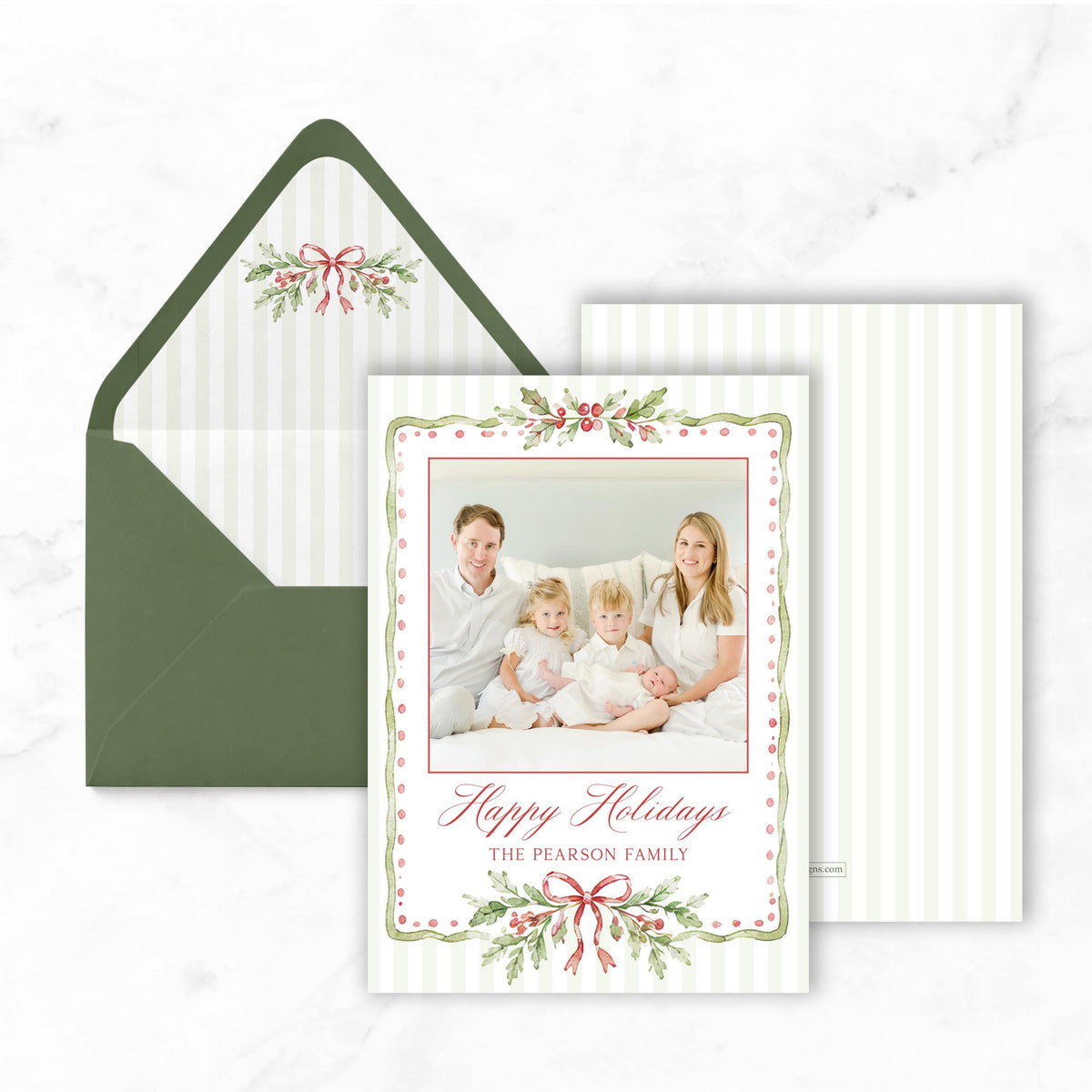 A green envelope with a white and red holiday card inside, featuring a family portrait of a man, woman, and child.