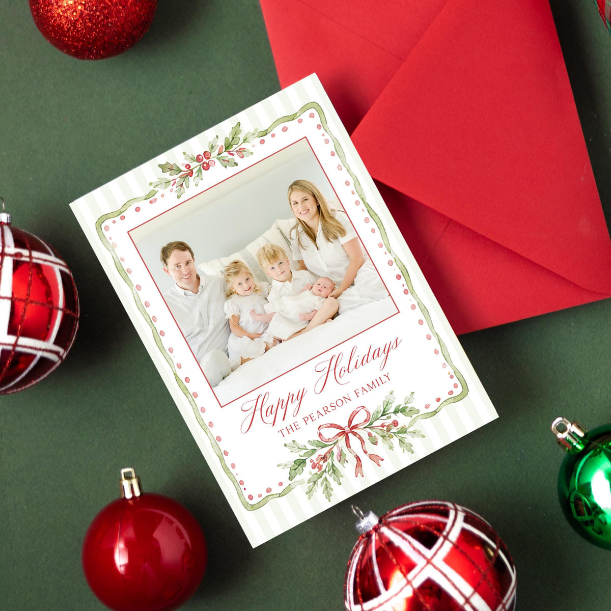 a Christmas card with a family photo, surrounded by ornaments and a red ribbon on a green background.