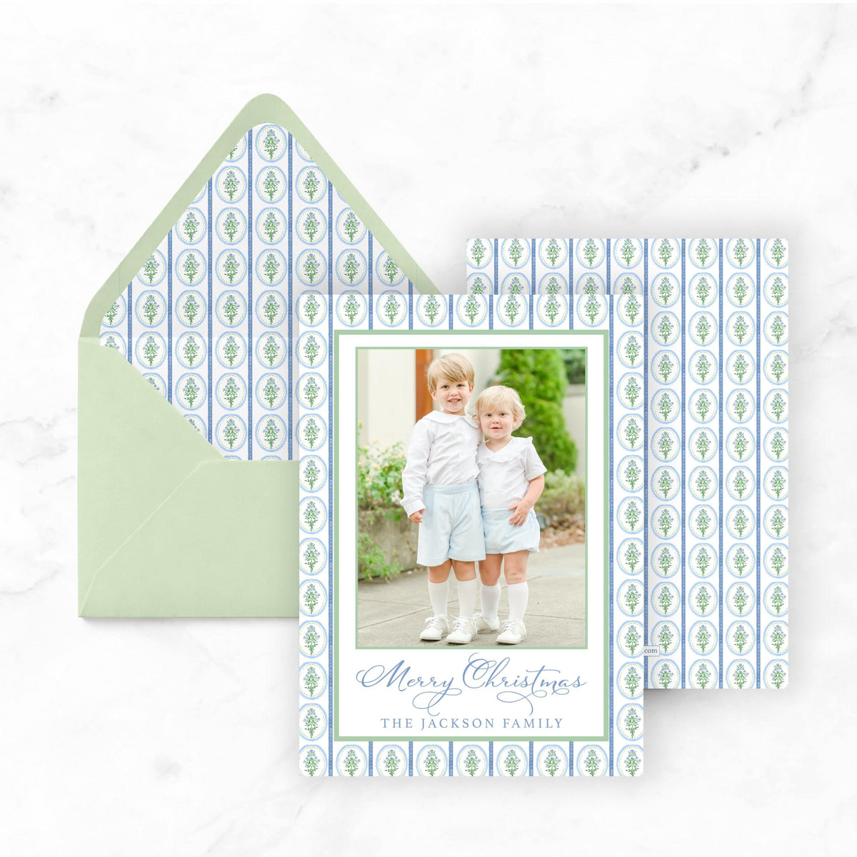 A Christmas card featuring two young boys in a family photo, with a green envelope and a patterned background.