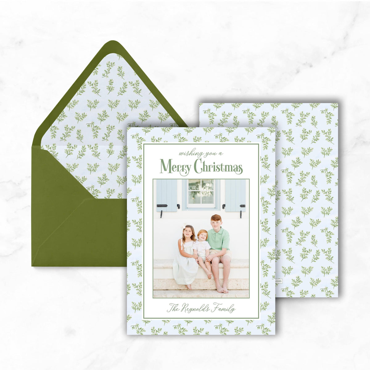 A green envelope with a white pattern and a greeting card featuring a family photo.
