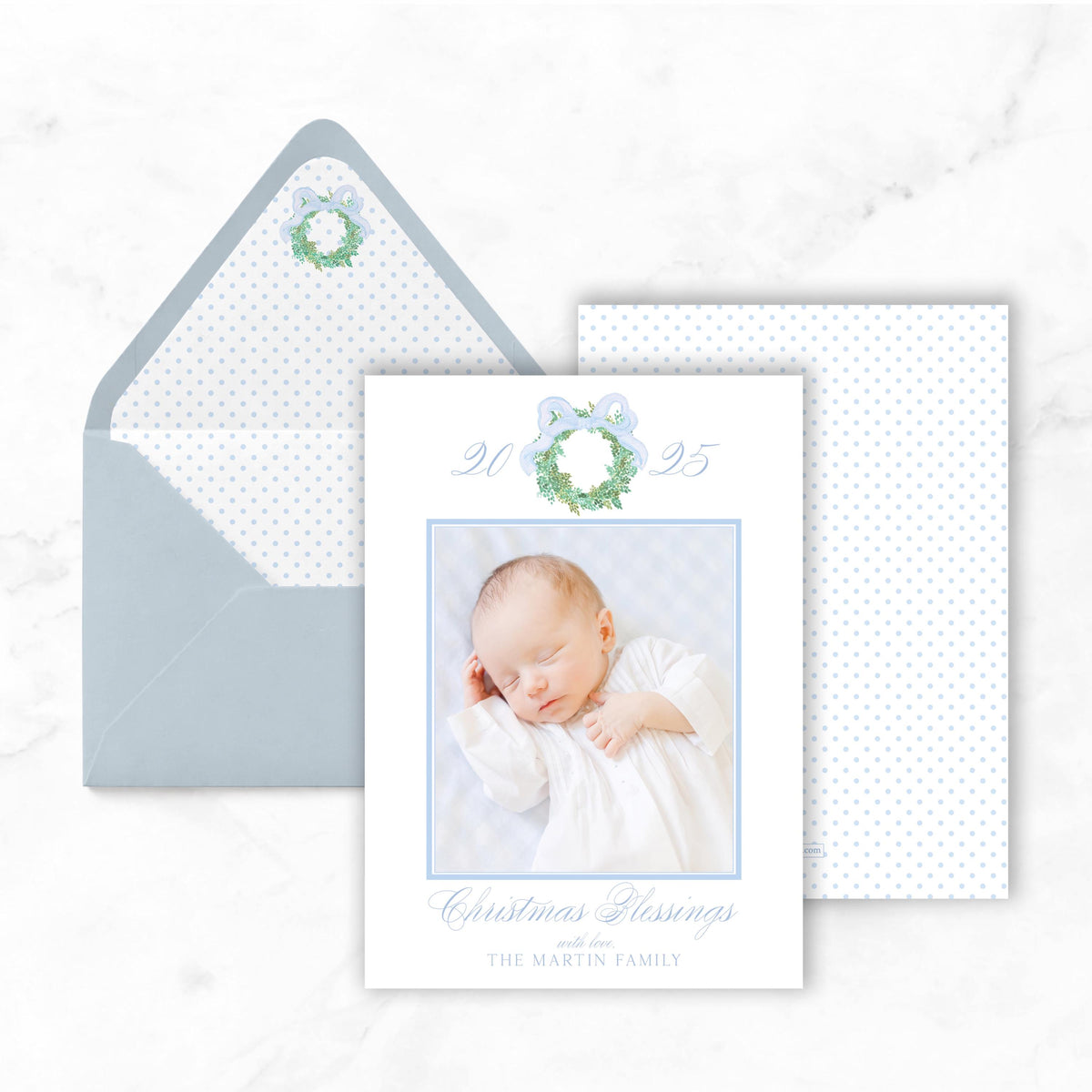 A white card with a photo of a sleeping baby, a blue ribbon, and text that reads "Christmas Blessings with The Martin Family".
