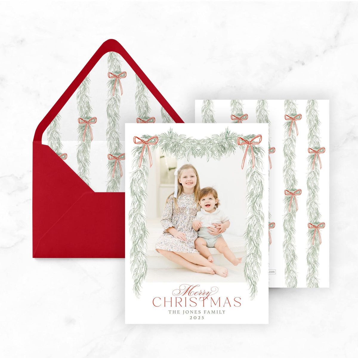 A Christmas card featuring two young girls sitting on a step, with a red envelope and a patterned paper below the card.