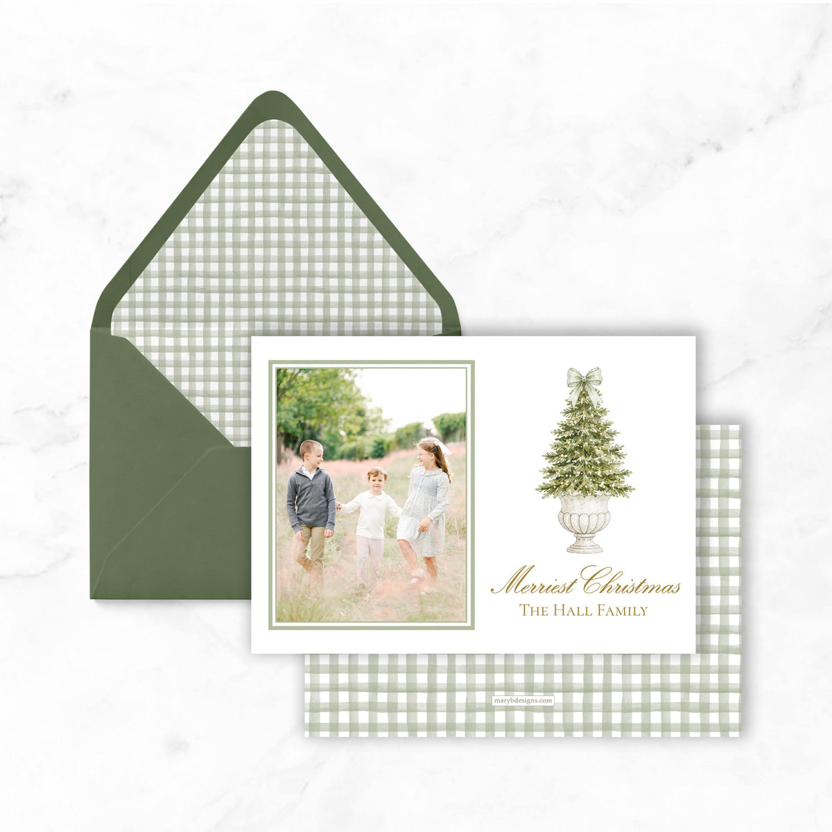 A green envelope with a white card inside, featuring a family photo and a Christmas tree illustration.