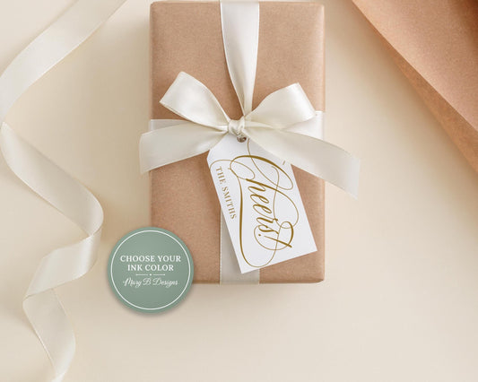 A gift box with a white ribbon and a tag that says "Cheers" is placed on a white surface.