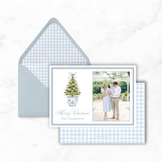 A blue and white checkered envelope with a holiday-themed card inside, featuring a family photo and a Christmas tree illustration.