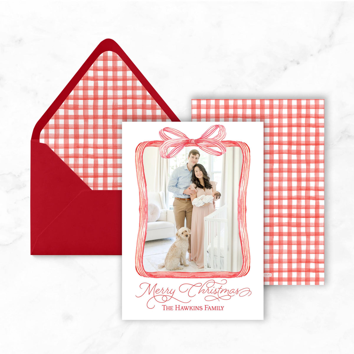 A Christmas card with a red bow and a photo of a couple, along with an envelope and a red and white checkered background.