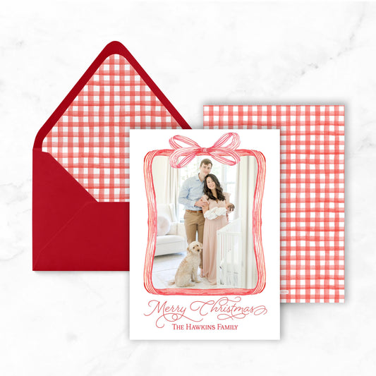 A Christmas card with a red bow and a photo of a couple, along with an envelope and a red and white checkered background.
