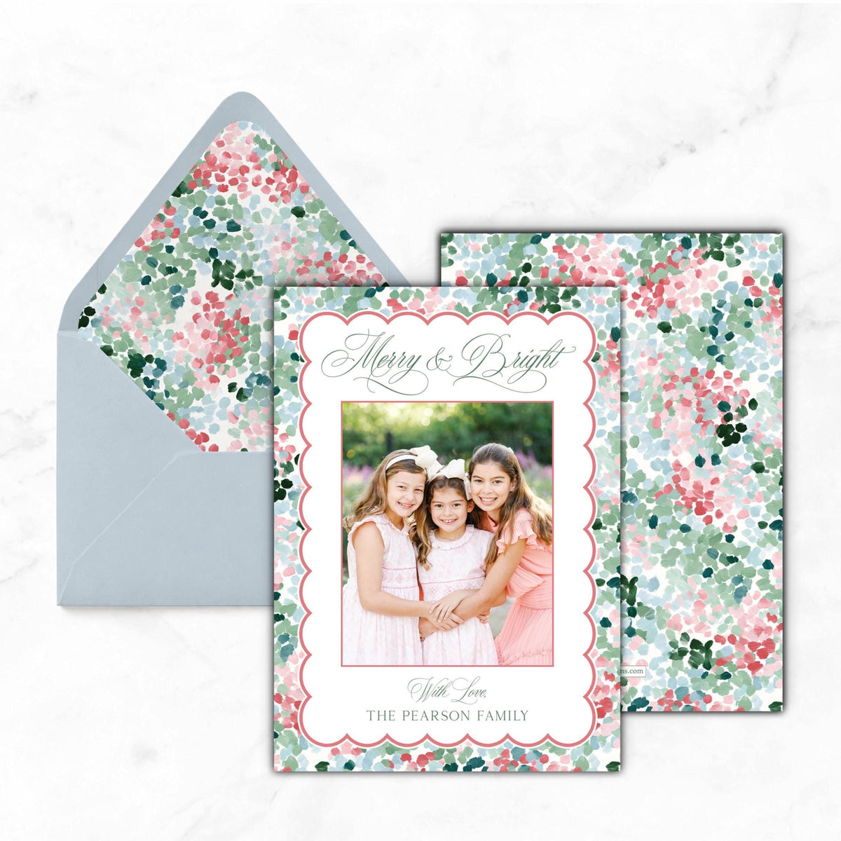 A holiday card featuring three young girls in pink dresses, with a floral pattern on the envelope and a photo of the girls in the center.