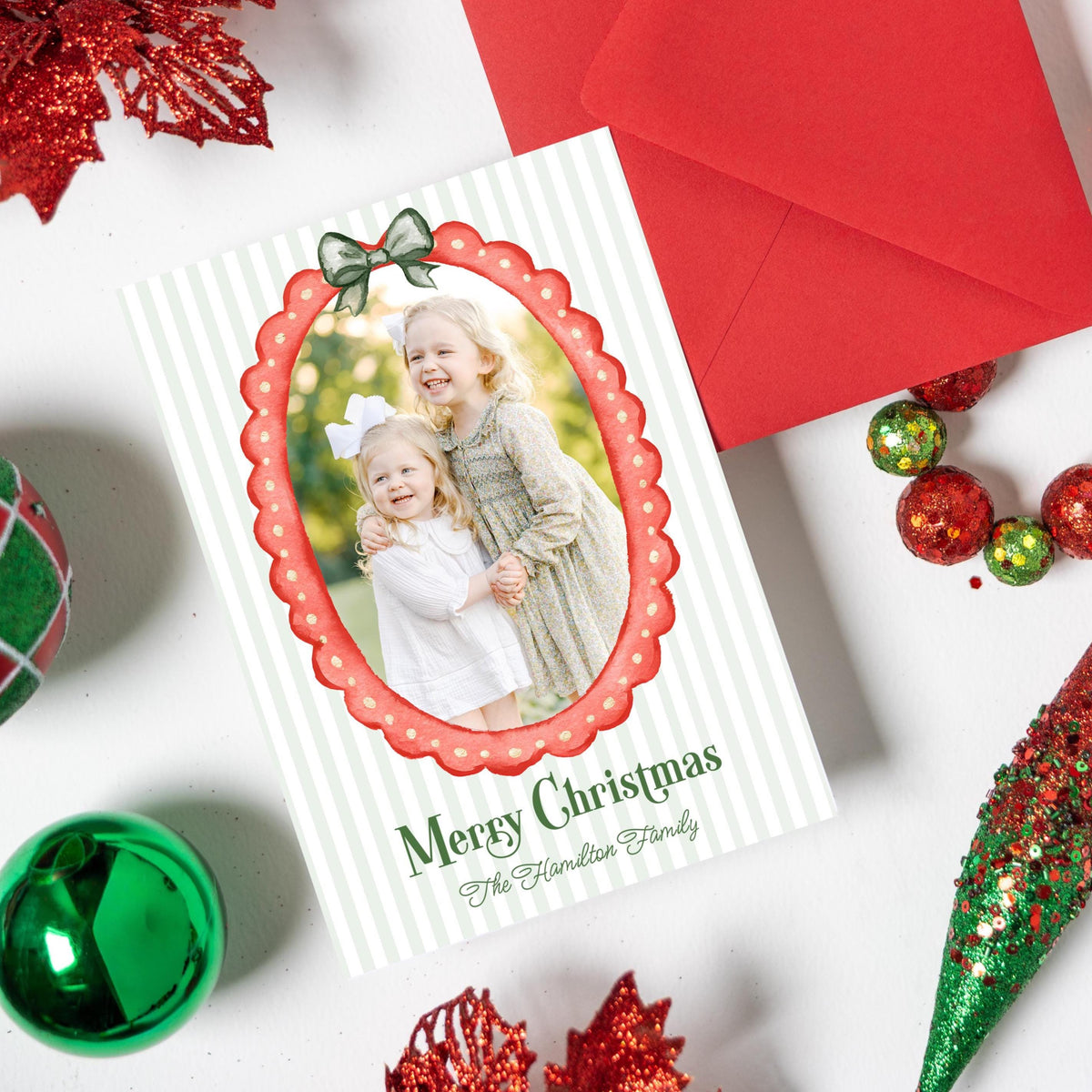 a Christmas card with a photo of two young girls, surrounded by various holiday decorations such as ornaments, tinsel, and a garland.