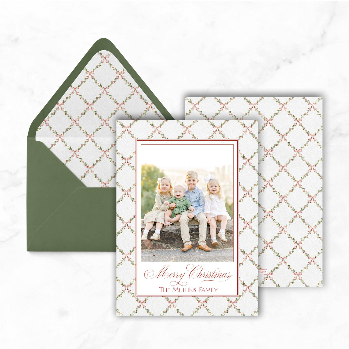 A Christmas card featuring a family photo with three children sitting together, placed on top of an envelope with a green lining.