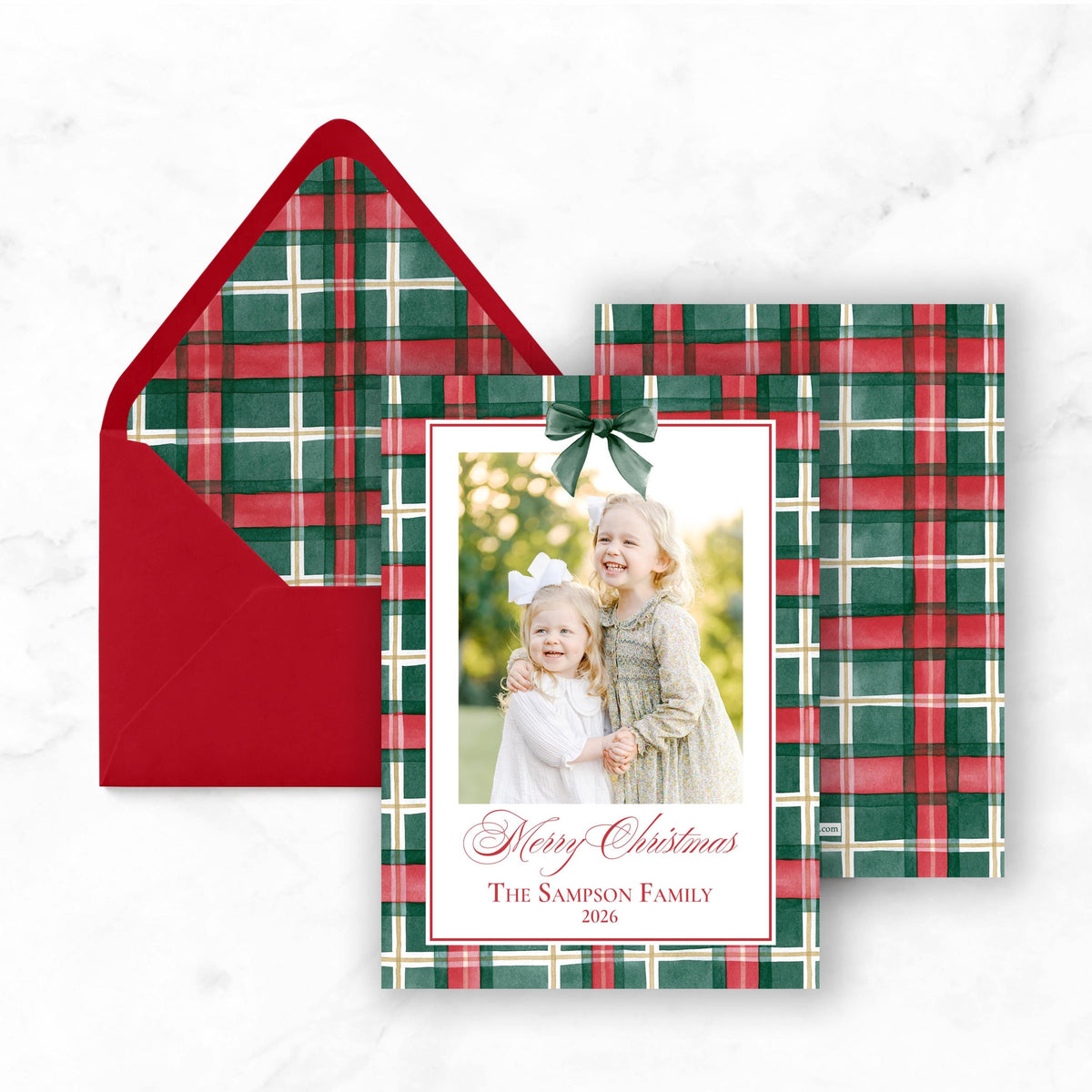 A Christmas card with a red envelope and a photo of two young girls smiling.