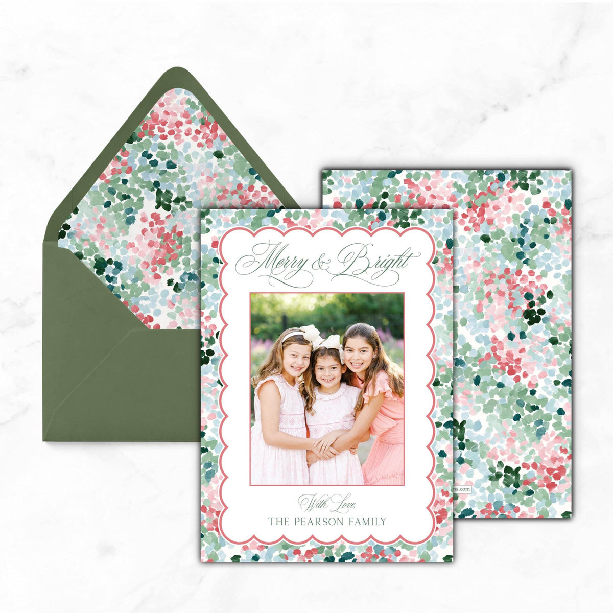A holiday card featuring three young girls in a floral print, with a green envelope and a matching floral print background.