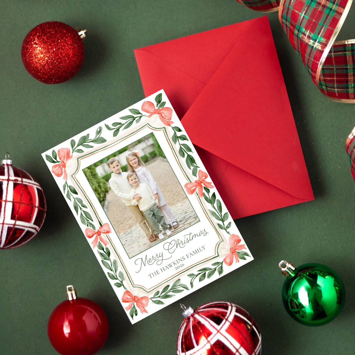 a Christmas card with a photo of a family, surrounded by ornaments and a red ribbon.