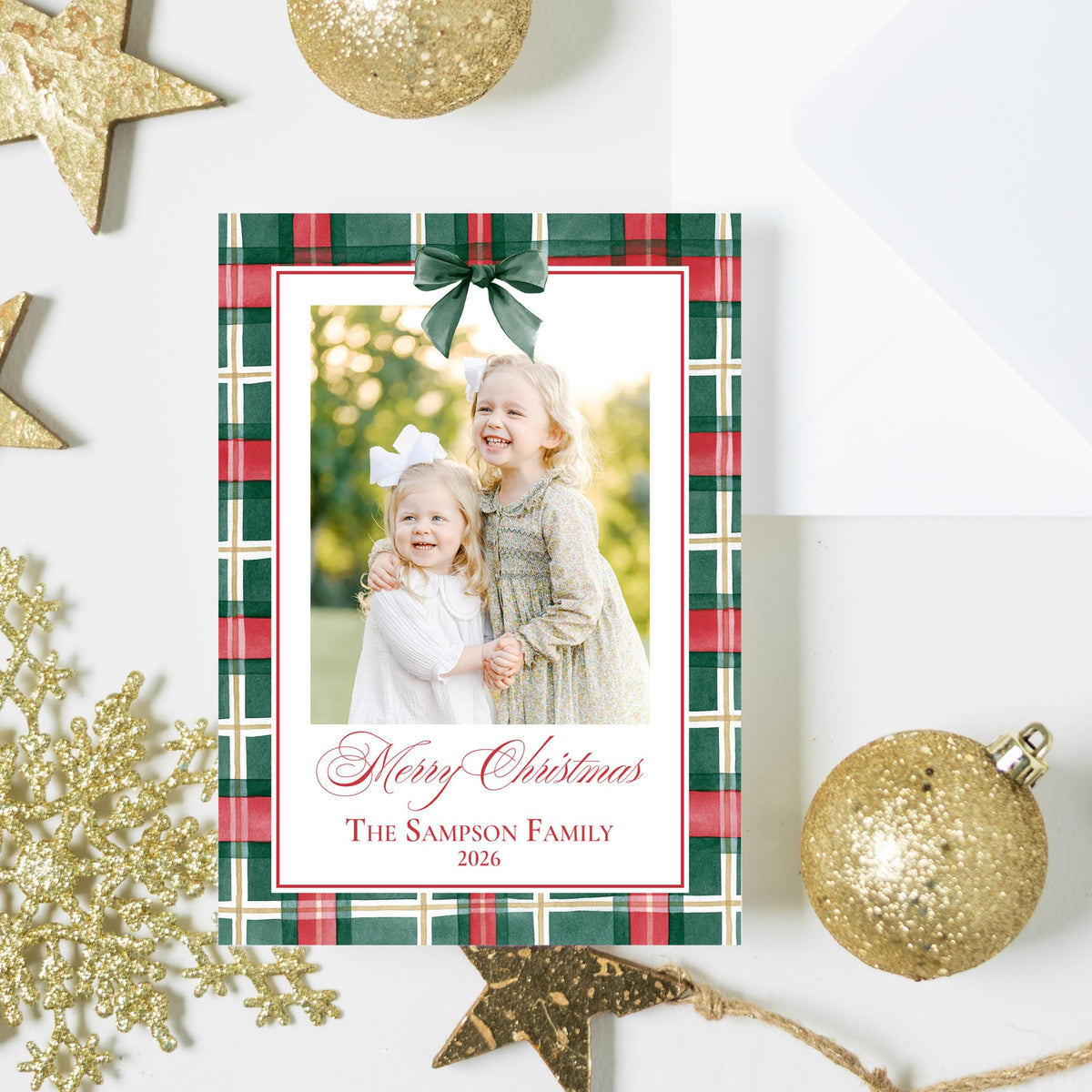 a festive arrangement of Christmas decorations, including gold glitter ornaments, star-shaped decorations, and a framed photo of two young girls.