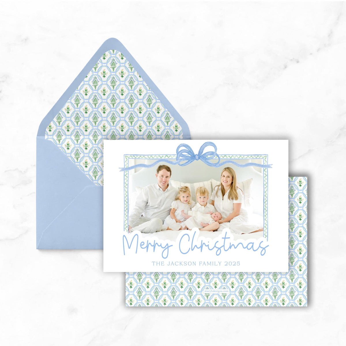 A Christmas card featuring a family photo with a bow, placed on top of an envelope with a patterned design.