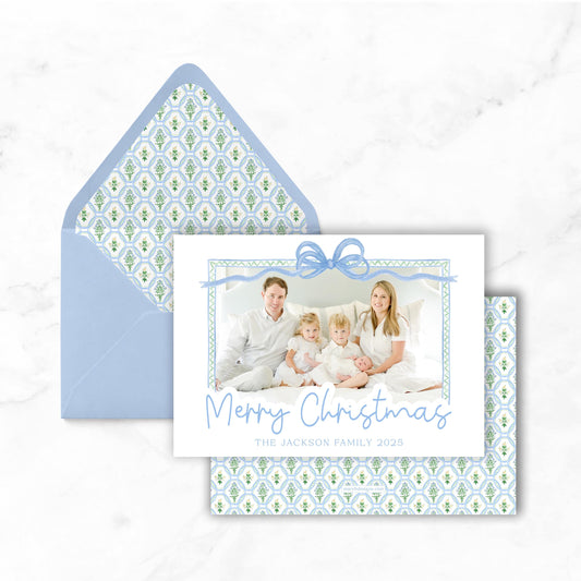 A Christmas card featuring a family photo with a bow, placed on top of an envelope with a patterned design.