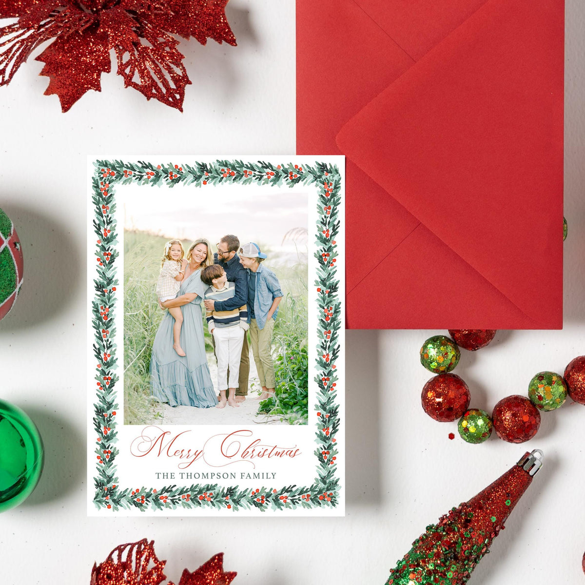 a festive arrangement of Christmas decorations, including ornaments, a red envelope, and a family photo, all set against a white background.