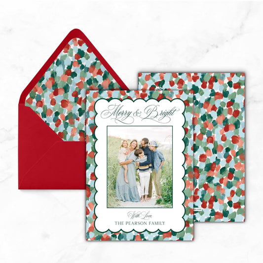 A holiday card featuring a family photo with the text "Merry & Bright" and "With Love, The Pearson Family" displayed on it. The card is placed next to a red envelope with a floral pattern.