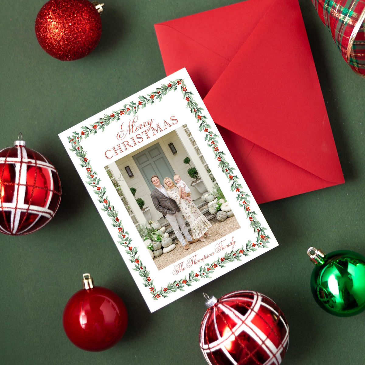 a Christmas card with a photo of a family, surrounded by ornaments and a red envelope on a green background.