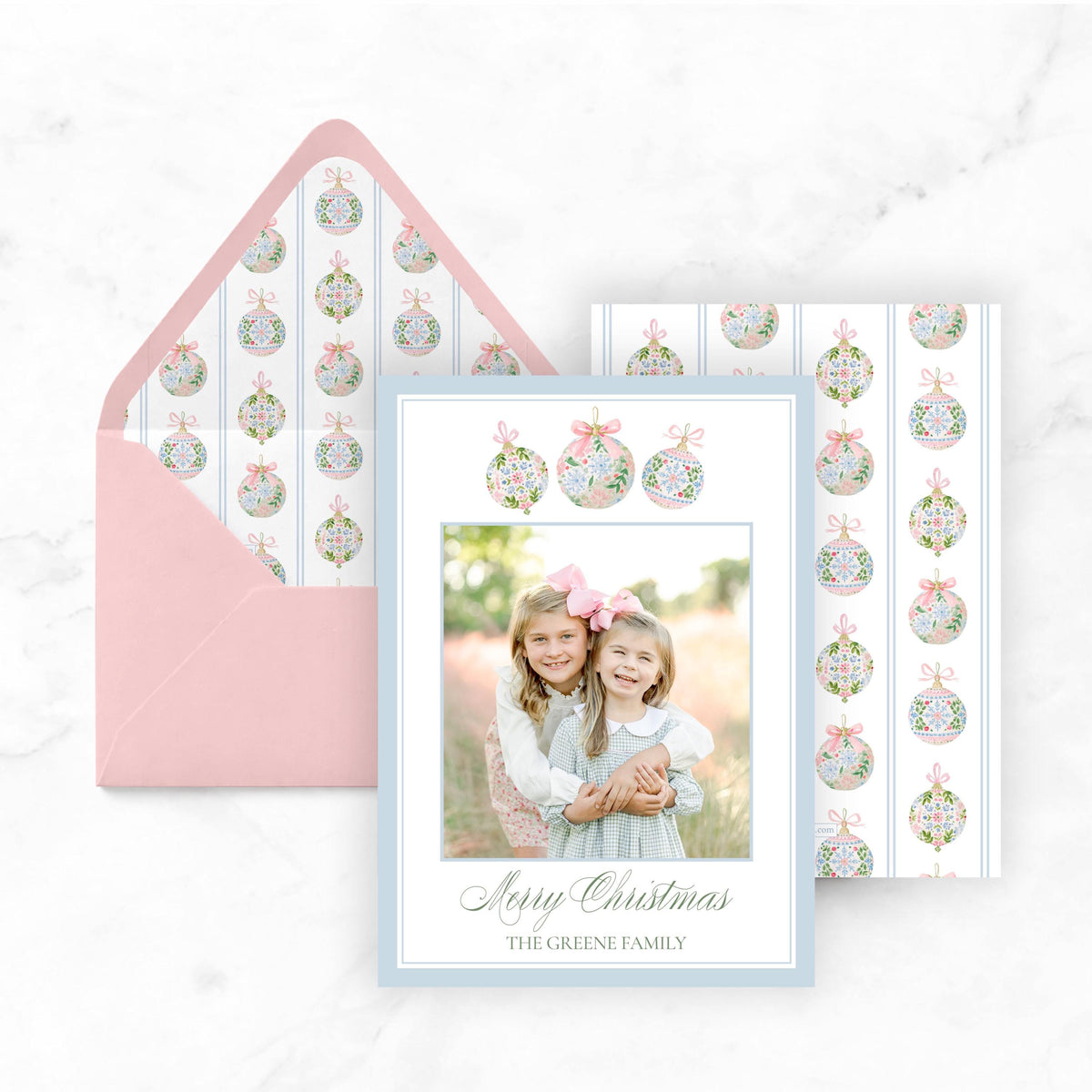A pink envelope with a photo of two young girls inside, along with a matching card featuring a photo of the same two girls.