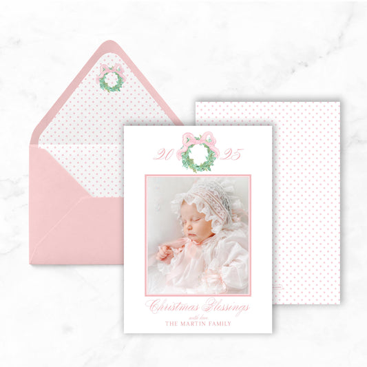 A pink and white Christmas card featuring a photo of a baby, with the text "Christmas Blessings The Martin Family" and a wreath design.