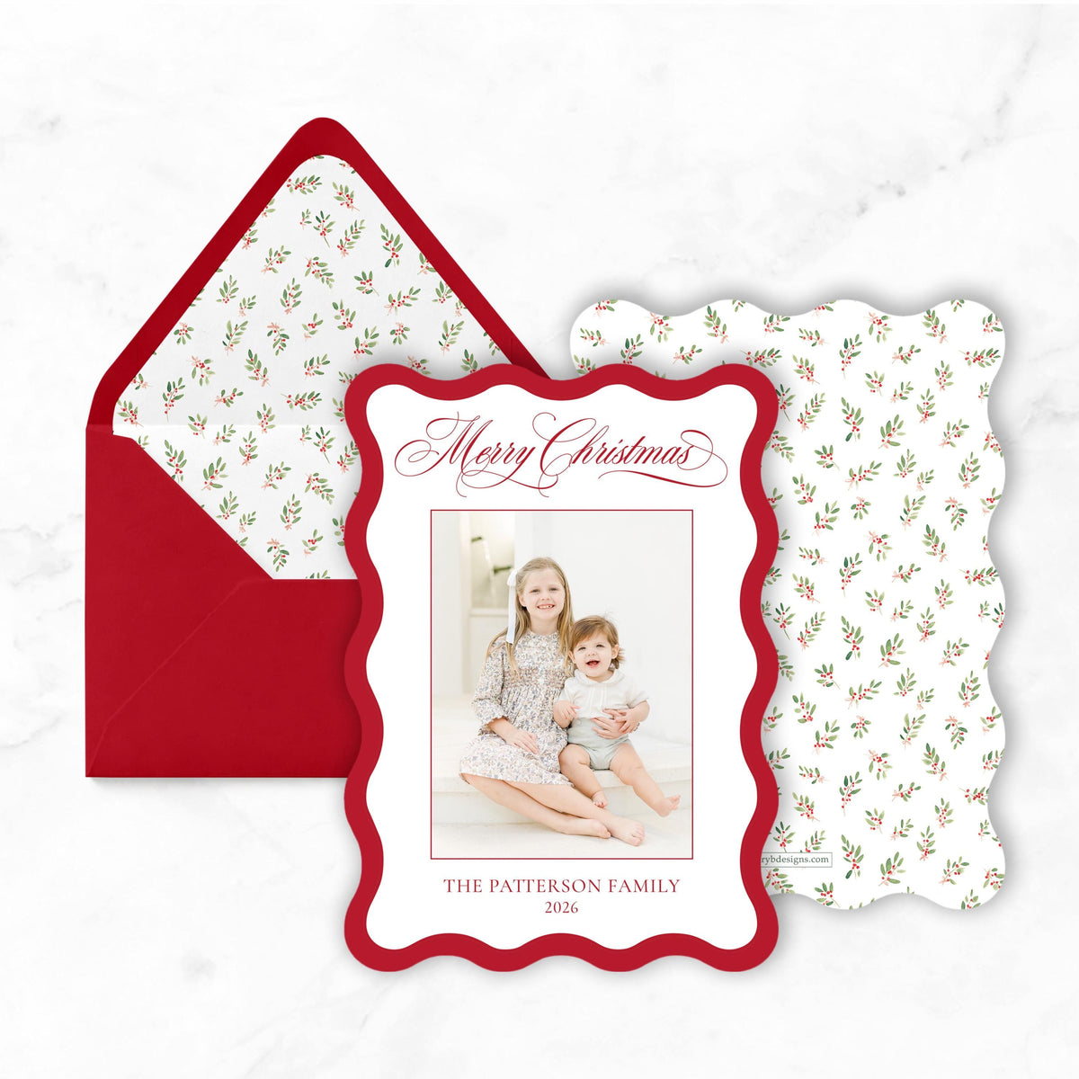 A red and white Christmas card with a photo of two women and a child, placed on a marble surface.