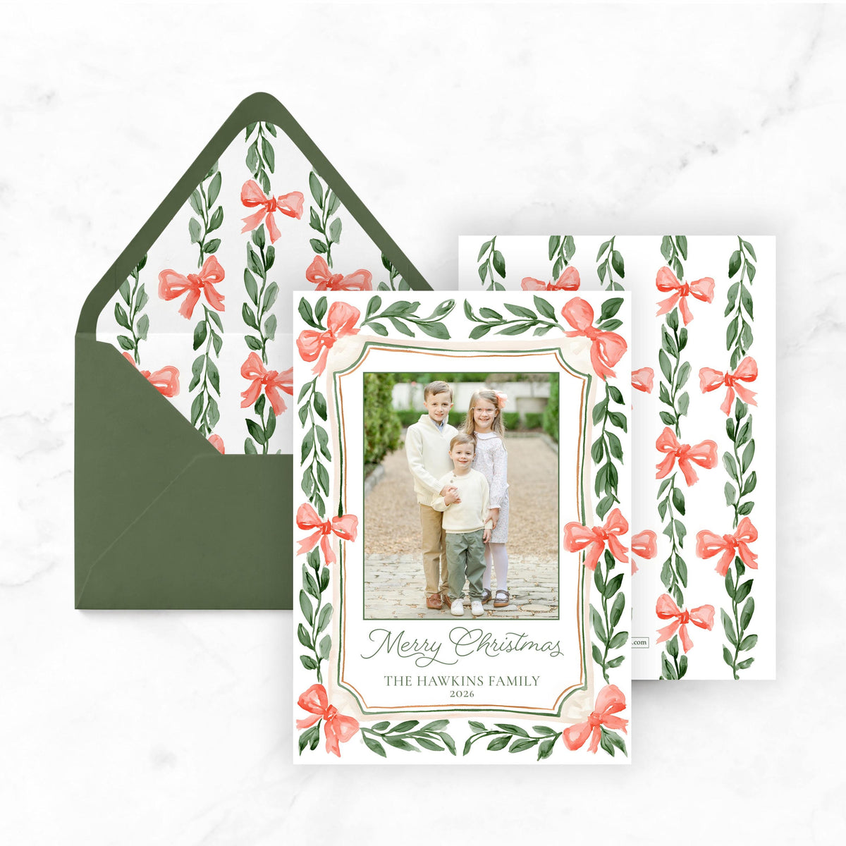 A holiday-themed card with a photo of three children and a bow design, placed on top of an envelope with a matching bow design.