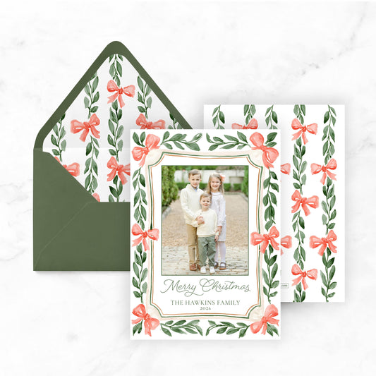 A holiday-themed card with a photo of three children and a bow design, placed on top of an envelope with a matching bow design.