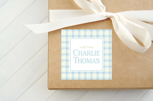 May include: A brown gift box with a white ribbon tied around it. The box has a blue and white checkered gift tag that says 'a gift from CHARLIE THOMAS'.
