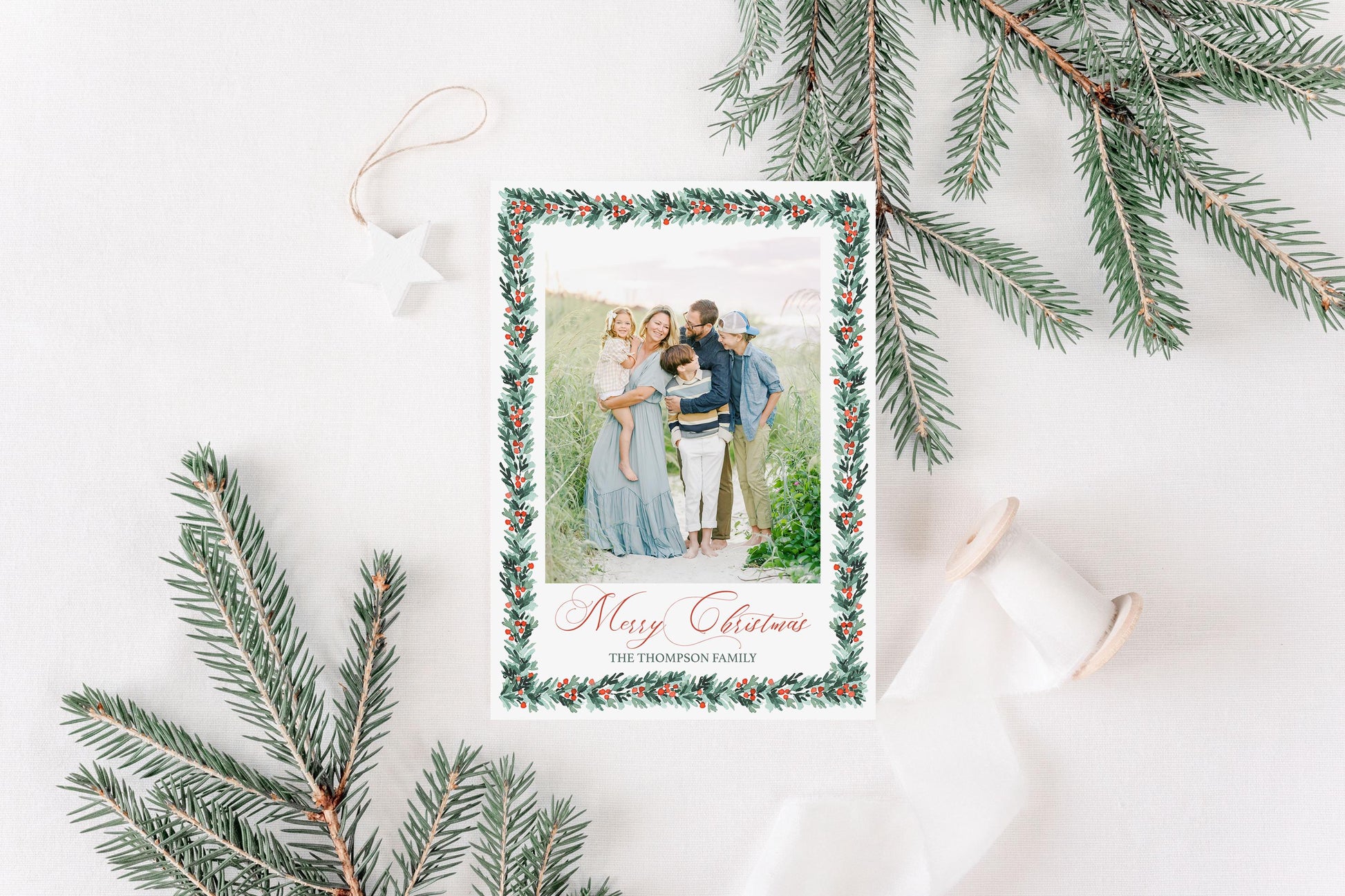 A Christmas card with a family photo is surrounded by pine branches and a star ornament, creating a festive holiday scene.