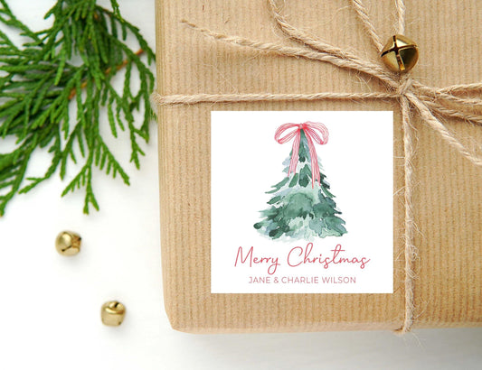 May include: A white gift tag with a watercolor illustration of a green Christmas tree with a pink bow. The text on the tag reads 'Merry Christmas' and 'Jane & Charlie Wilson'.