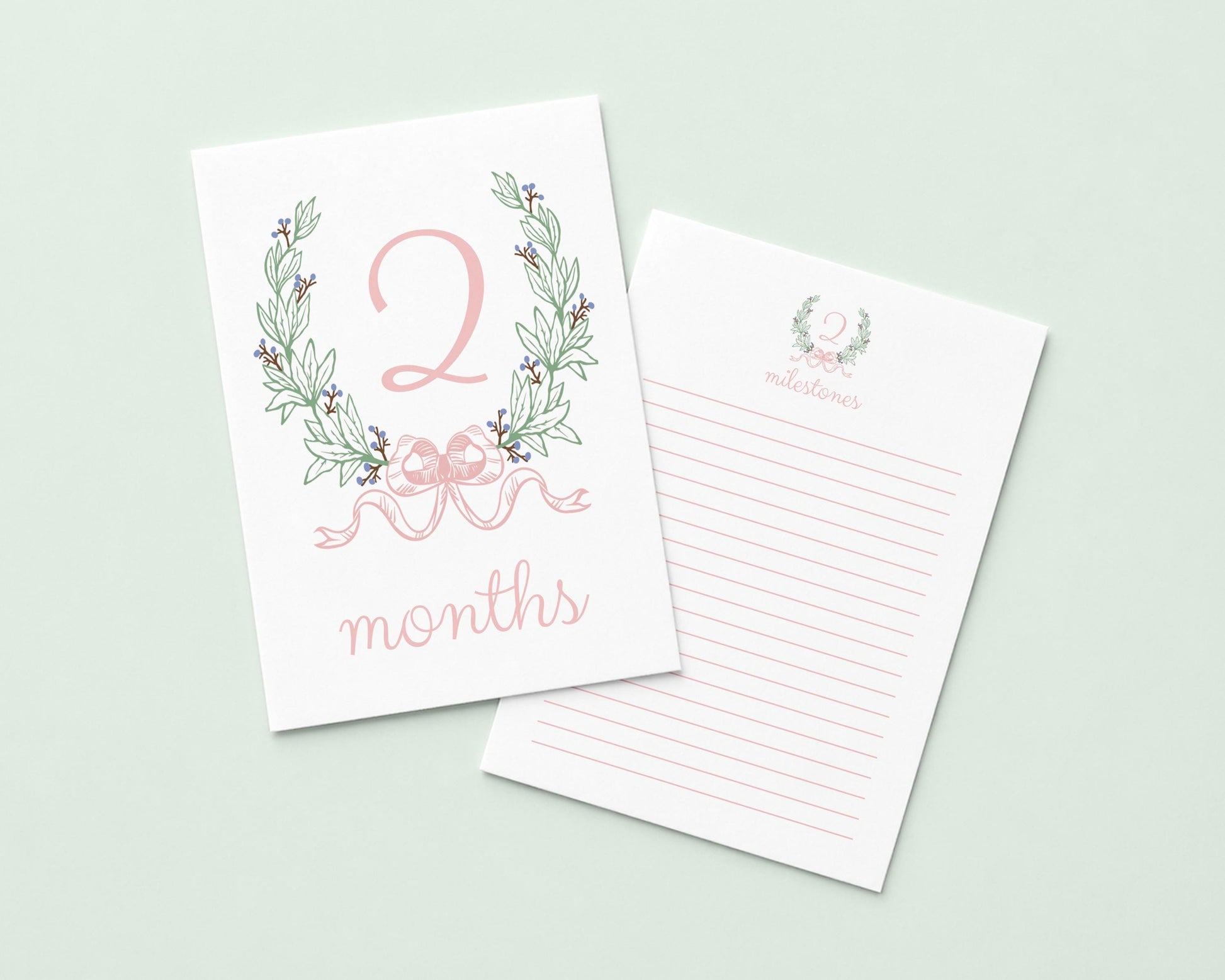 a white card with a pink floral design and the number "2" on it, along with the text " Months" written below. The card is placed next to a blank lined paper, suggesting it could be used for writing or note-taking.