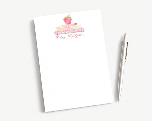 A white notepad with a watercolor illustration of a stack of books and an apple on top, along with the text "Mrs. Mason".