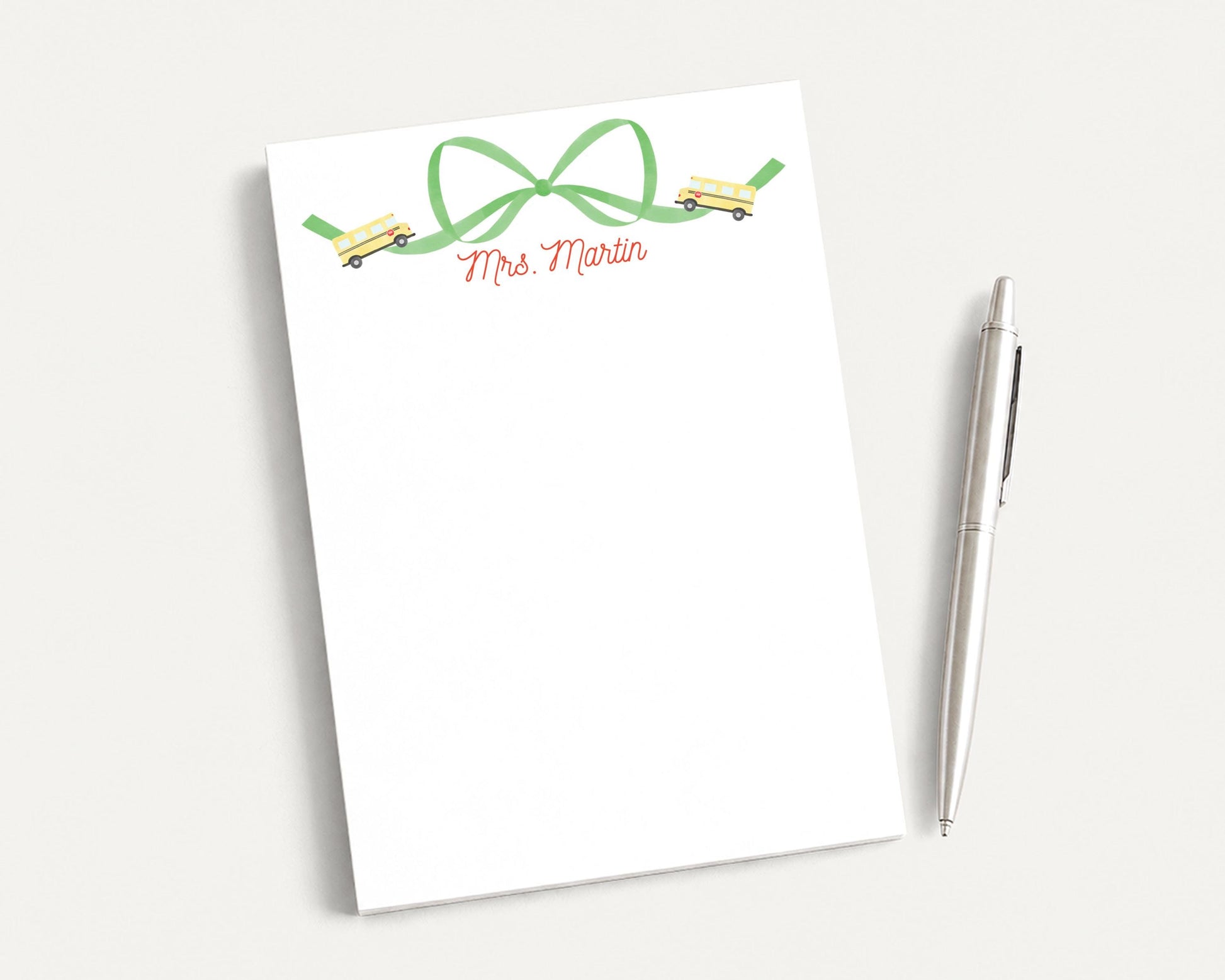 A white notepad with a green bow and a pen on a white surface.