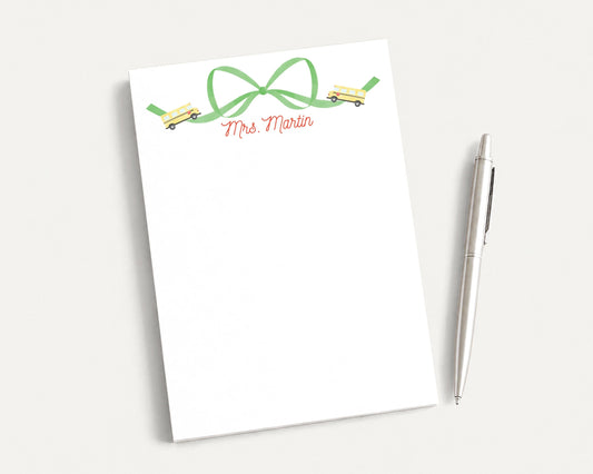 A white notepad with a green bow and a pen on a white surface.