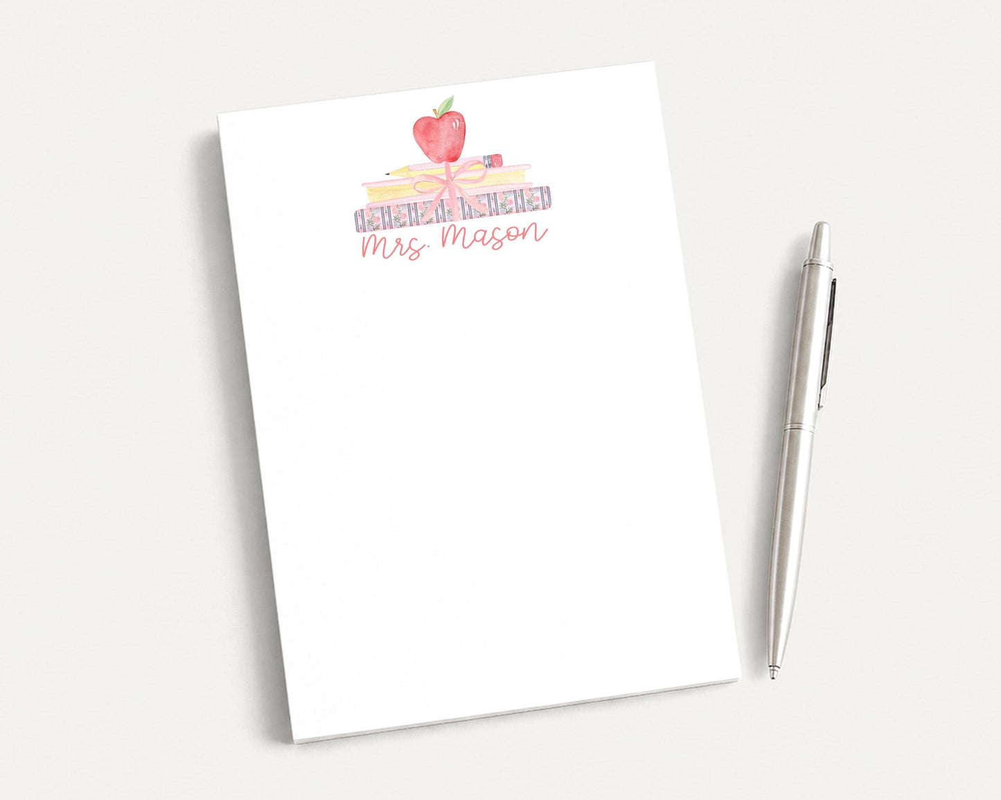 A white notepad with a watercolor illustration of a stack of books and an apple on top, along with the text "Mrs. Mason".