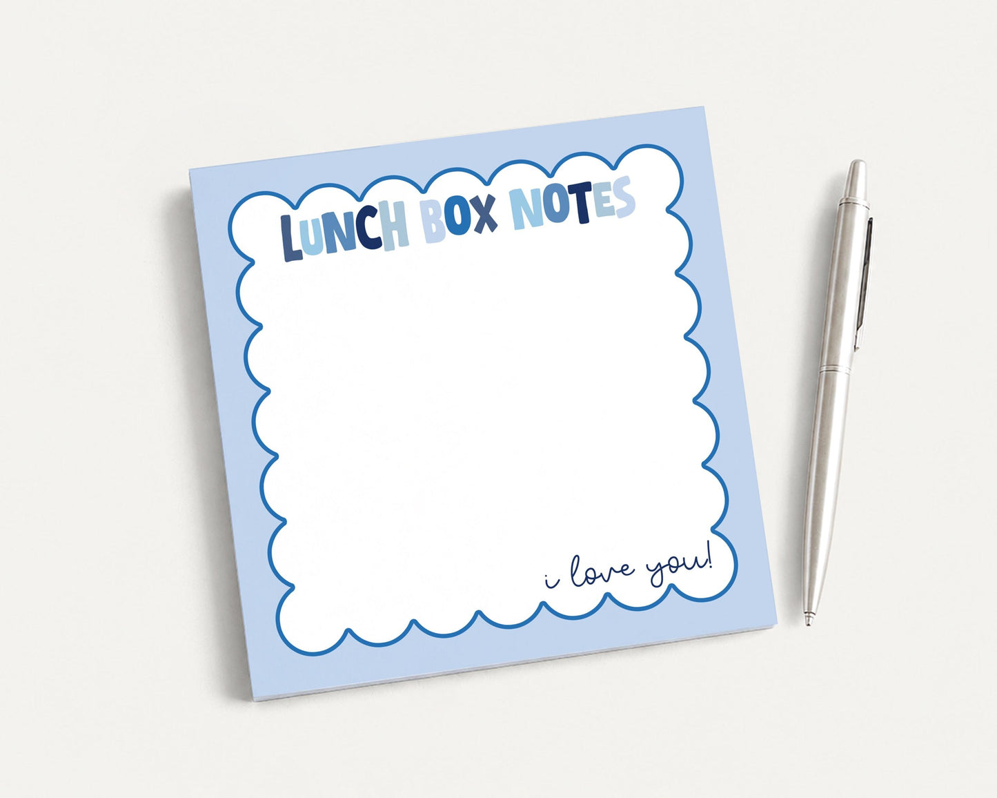 A blue and white lunch box note pad with a pen next to it.